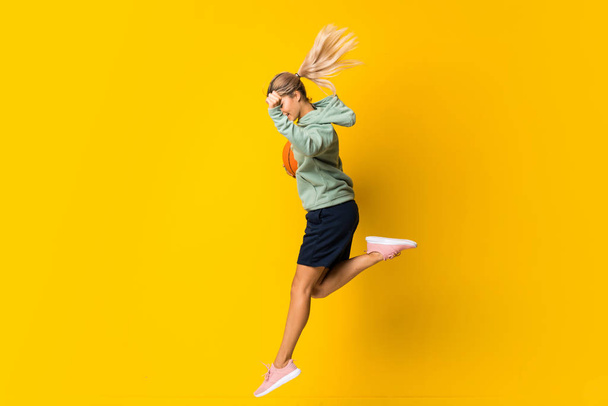 Teenager girl basketball ball jumping over isolated yellow background - Photo, Image