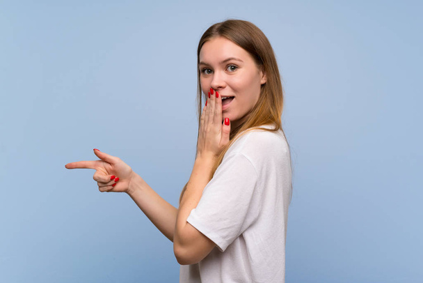 Jovem mulher sobre a parede azul apontando o dedo para o lado com um rosto surpreso
 - Foto, Imagem