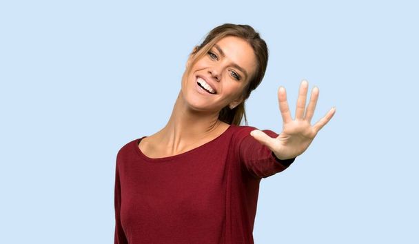 Blonde vrouw tellen vijf met vingers over geïsoleerde blauwe achtergrond - Foto, afbeelding