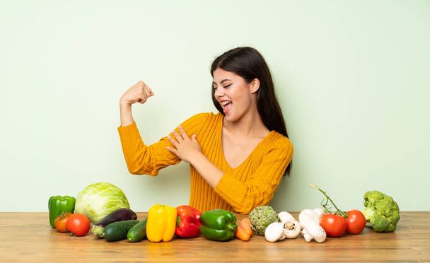 Teenager girl with many vegetables doing strong gesture - Photo, Image
