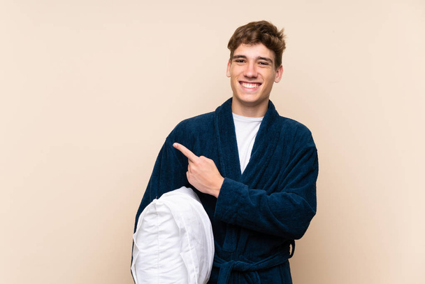 Jóképű fiatalember pizsamában több mint elszigetelt fal mutatva az oldalon, hogy nyújtson be egy termék - Fotó, kép