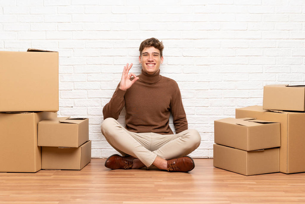 Guapo joven que se mueve en un nuevo hogar entre cajas que muestran un signo de ok con los dedos
 - Foto, Imagen