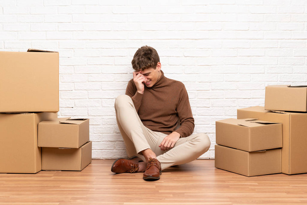Όμορφος νέος άντρας που μετακομίζει σε νέο σπίτι ανάμεσα σε κουτιά γελώντας - Φωτογραφία, εικόνα