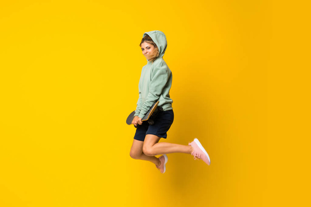 Szőke tinédzser korcsolyázó lány ugrott át elkülönített sárga háttér - Fotó, kép