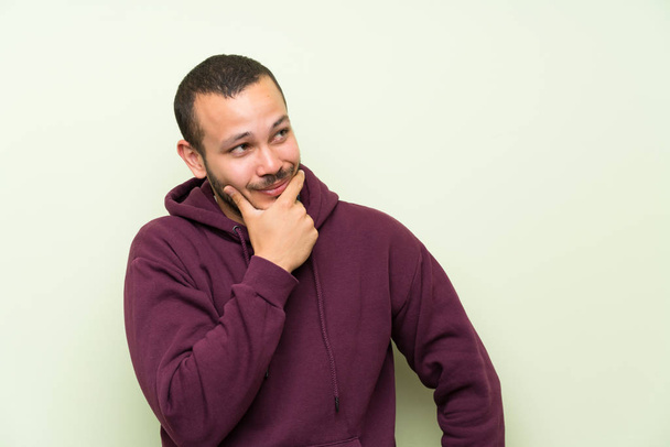 Colombian man with sweatshirt over green wall thinking an idea - Foto, Imagem