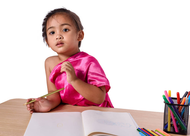 Cute cheerful child drawing using color pencil while sitting at  - Foto, Imagen