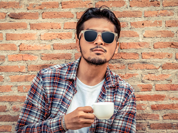 Junger Mann hält Kaffeetasse gegen Ziegelwand. - Foto, Bild
