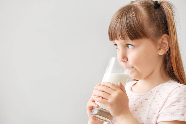 Aranyos kis lány pohár tejet világos háttér - Fotó, kép