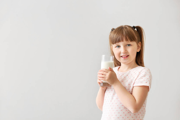 χαριτωμένο μικρό κορίτσι με το ποτήρι γάλα επάνω ελαφρύς υπόβαθρο - Φωτογραφία, εικόνα