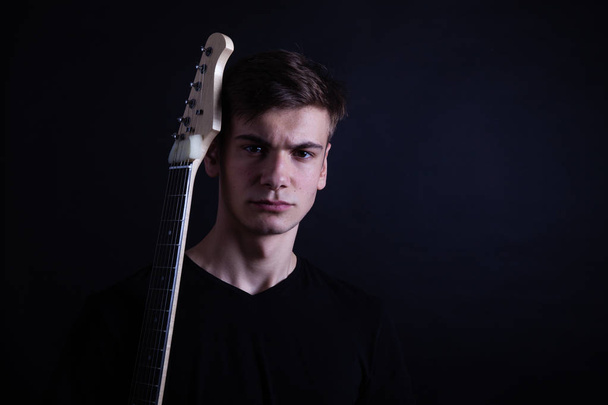 Young caucasian adult posing with electric guitar in the studio. Black isolated background - 写真・画像
