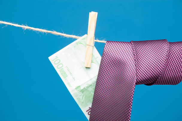 Dinero colgado de una cuerda sostenida por pinzas de madera, junto con material textil, una corbata hecha con billetes de euro
. - Foto, Imagen