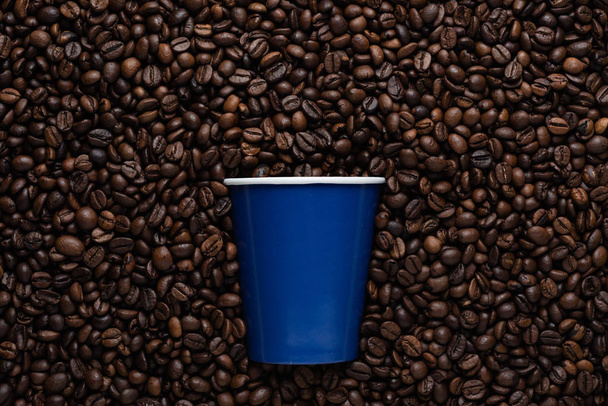 Blue disposable cup of coffee to go on the background of roasted beans. - Photo, Image