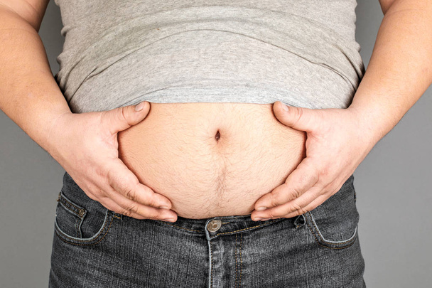 dikke man, het controleren van zijn gewicht, op een grijze achtergrond - Foto, afbeelding