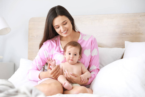 glückliche Mutter mit entzückendem Baby, das zu Hause auf dem Bett sitzt - Foto, Bild
