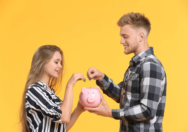 Casal feliz colocando moedas no banco porquinho no fundo de cor
 - Foto, Imagem