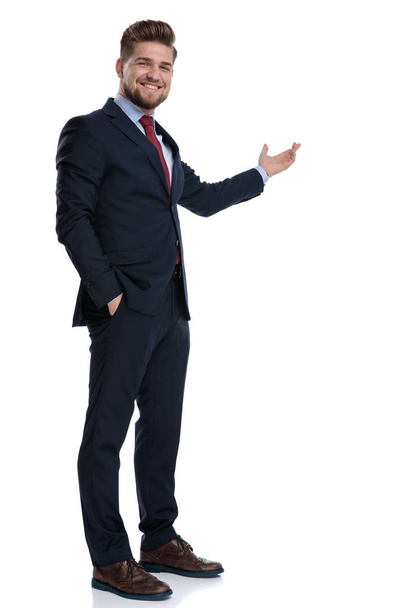 Positive businessman presenting and holding his hand in his pock - Foto, afbeelding