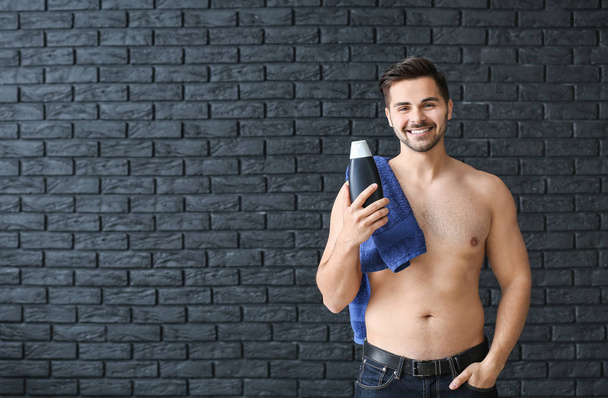 Handsome man with bottle of shampoo and towel on dark background - Photo, Image