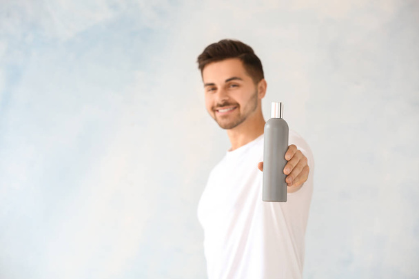 Knappe man met fles shampoo op lichte achtergrond - Foto, afbeelding