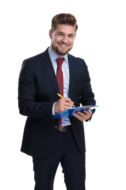Happy businessman smiling and writing on his clipboard  - Φωτογραφία, εικόνα