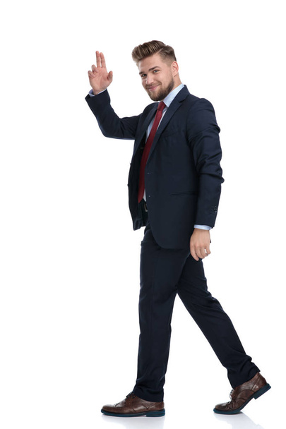 Vista lateral de un hombre de negocios caminando y saludando
 - Foto, imagen