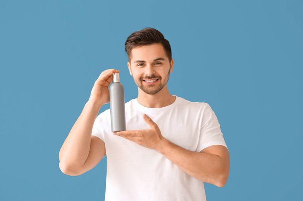 Handsome man with bottle of shampoo on color background - Foto, afbeelding