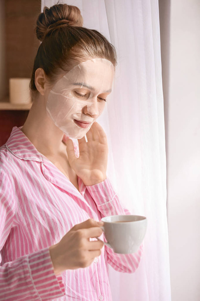 Молодая женщина в маске для лица пьет чай дома
 - Фото, изображение