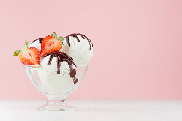 Summer cold dessert - three creamy ice cream balls with chocolate sauce, ripe strawberry slices in glass bowl on white wood table and pastel pink wall. - Photo, image