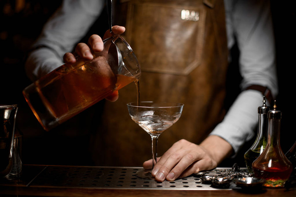 Bartender pouring an alcoholic drink from the measuring cup to the empty cocktail glass - 写真・画像