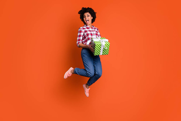 Full size photo of jumping high excited lady hold pack unexpected present boyfriend wear jeans denim pants plaid shirt isolated orange bright background - Φωτογραφία, εικόνα