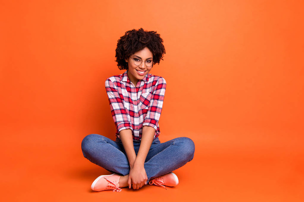 Full length body size photo beautiful nice she her dark skin lady sitting floor legs crossed amazing look wear specs casual jeans denim checkered plaid shirt isolated bright orange background - Photo, Image