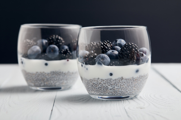 selective focus of yogurt with chia seeds, blueberries, blackberries on white wooden isolated on black - 写真・画像