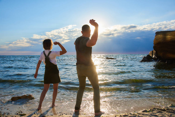 onnellinen rakastava pari tavata auringonnousun ja pelata rannalla valtameren rannalla. auringon häikäisy kehyksessä
 - Valokuva, kuva
