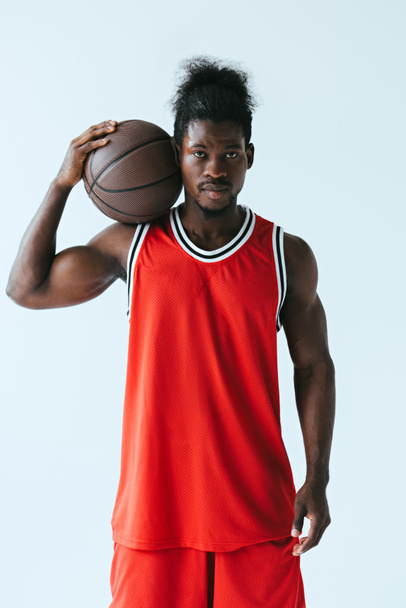 серьезный африканский американский спортсмен с баскетбольным мячом, смотрящий на камеру, изолированную на сером
 - Фото, изображение