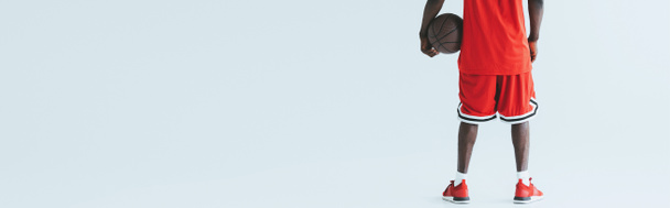 vue recadrée du joueur afro-américain de basket tenant le ballon sur fond gris, prise de vue panoramique
 - Photo, image
