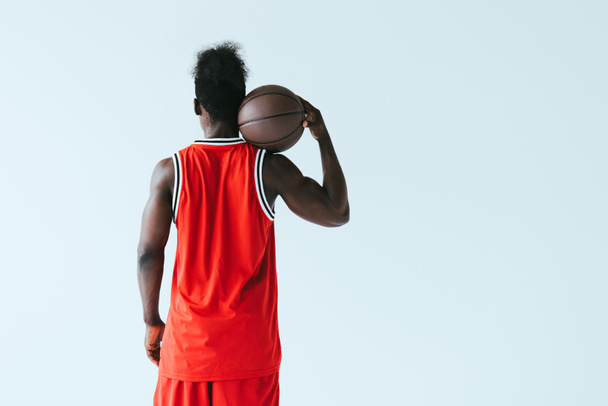 back view of african american basketball player in red sportswear holding ball isolated on grey - Fotoğraf, Görsel