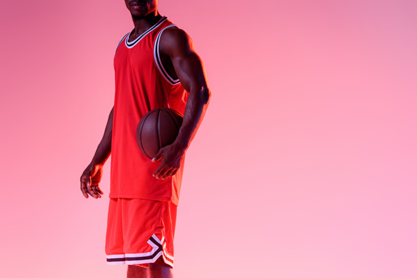 vista cortada do jogador de basquete americano africano segurando bola no fundo rosa com gradiente
 - Foto, Imagem