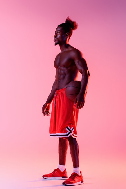 apuesto jugador de baloncesto afroamericano mirando hacia otro lado en rosa y púrpura degradado fondo con iluminación
  - Foto, Imagen