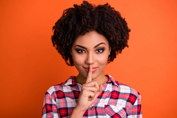 Close-up portrait of her she nice attractive lovely cheery wavy-haired lady in checked shirt showing shh sign conspiracy censorship isolated on bright vivid shine orange background - Фото, изображение
