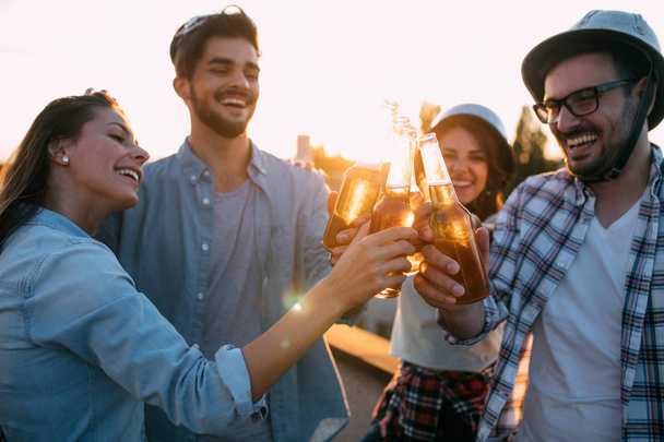 Friends having fun and drinking beer outdoor on a rooftop get together - Photo, image