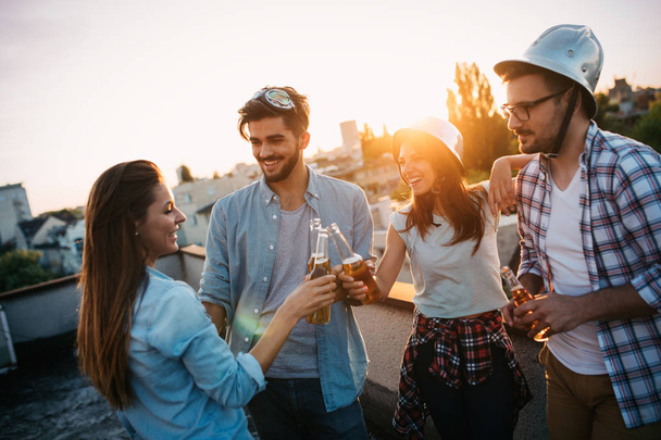 Young people partying on terrace with drinks at sunset. Young men and women enjoying drinks on rooftop - 写真・画像