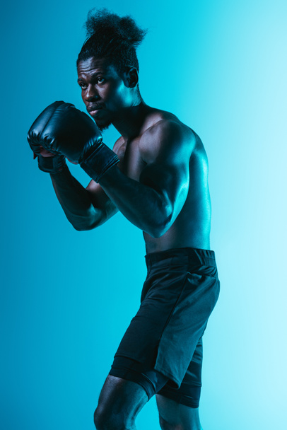 confident african american sportsman with muscular torso boxing on blue background - Zdjęcie, obraz