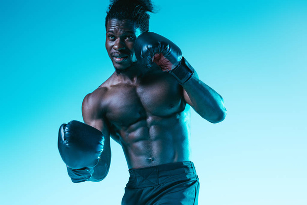 handsome, muscular african american sportsman boxing on blue background - Photo, Image