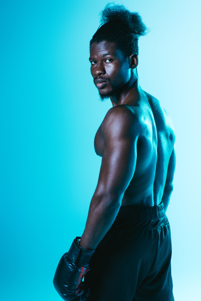 confident african american boxer with muscular torso looking at camera on blue background - Foto, Imagem
