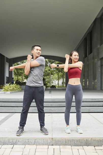 Wesoły młody Asian Mężczyzna i kobieta robi ćwiczenia do Stretch Arms  - Zdjęcie, obraz