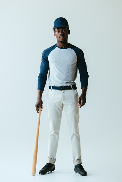 schöner afrikanisch-amerikanischer Baseballspieler posiert vor der Kamera auf grauem Hintergrund - Foto, Bild