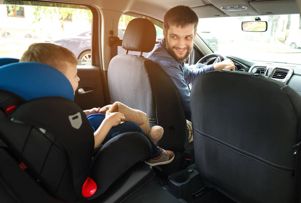 Uomo guida auto con il figlio allacciato sul seggiolino
 - Foto, immagini