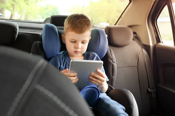 Мальчик с планшетным компьютером, пристегнутым к автомобильному креслу
 - Фото, изображение