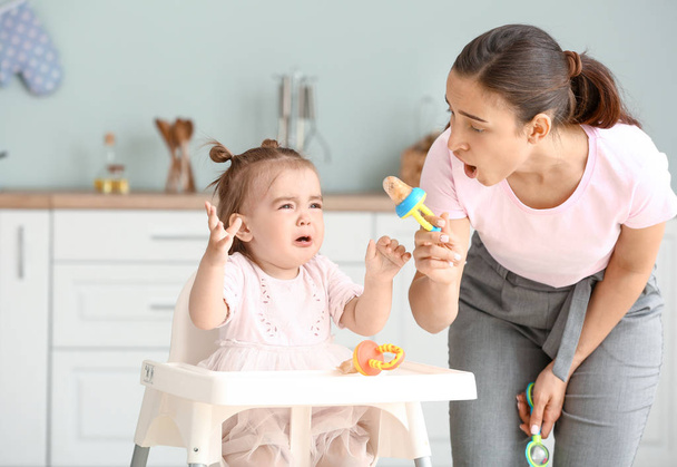 Mother giving her little daughter nibbler with tasty food in kitchen at home - Photo, image