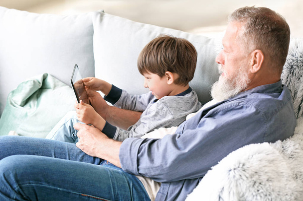 Cute little boy and his grandfather with tablet computer at home - 写真・画像