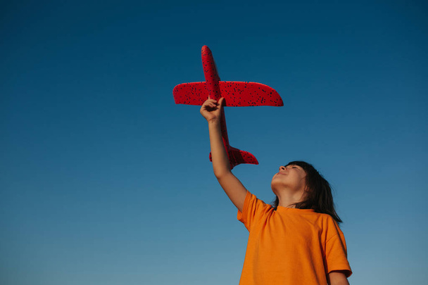 happy little girl holds in your hand a red plane, outdoors, sky background, copy space - Photo, Image